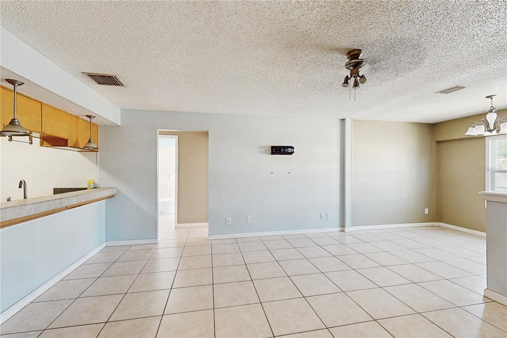 A spacious living area features light-colored tile flooring, a popcorn ceiling, and a kitchen pass-through — 117 N MERCURY AVENUE UNIT 117, CLEARWATER, FL