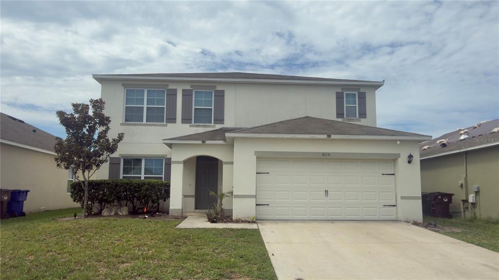 A two-story suburban house features a beige stucco exterior, a two-car garage, and a lawn — 5110 FIDDLEWOOD WAY, ST CLOUD, FL