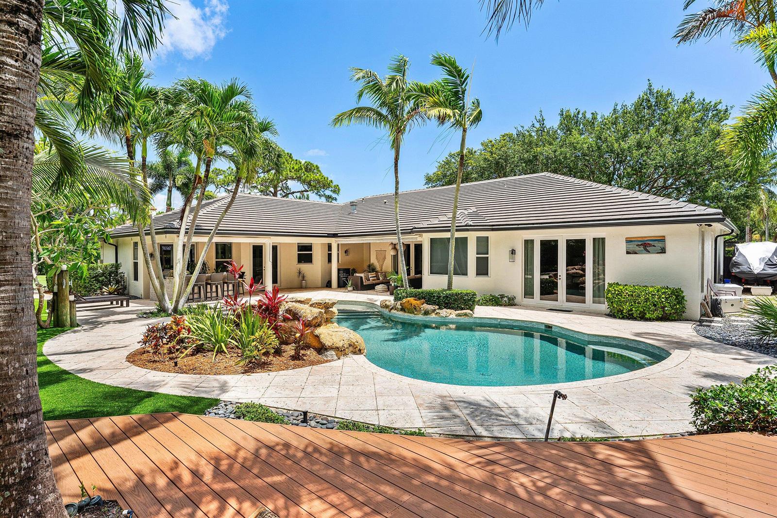 A backyard features a swimming pool, stone patio, tropical landscaping, and a single-story house — 1505 Addison Avenue, Boca Raton FL 33486, BOCA RATON, FL