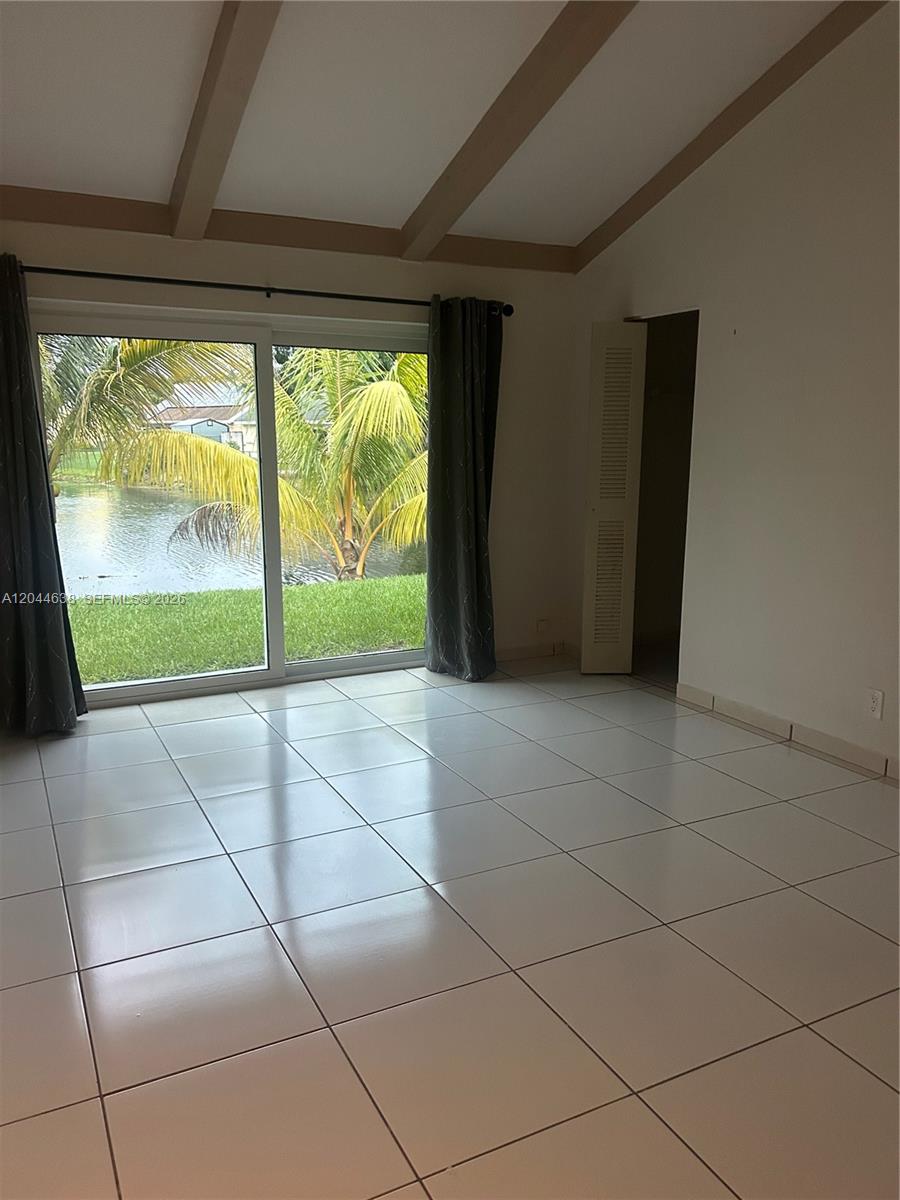 An empty room with white tile flooring, ceiling beams, and a sliding glass door view — 2730 Cypress Ave, Miramar FL 33025, MIRAMAR, FL