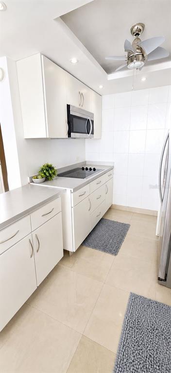 A kitchen features white cabinets, stainless steel appliances, light countertops, and a ceiling fan — 1607 AVENIDA JUAN PONCE DE LEON UNIT 1611, SANTURCE, PR