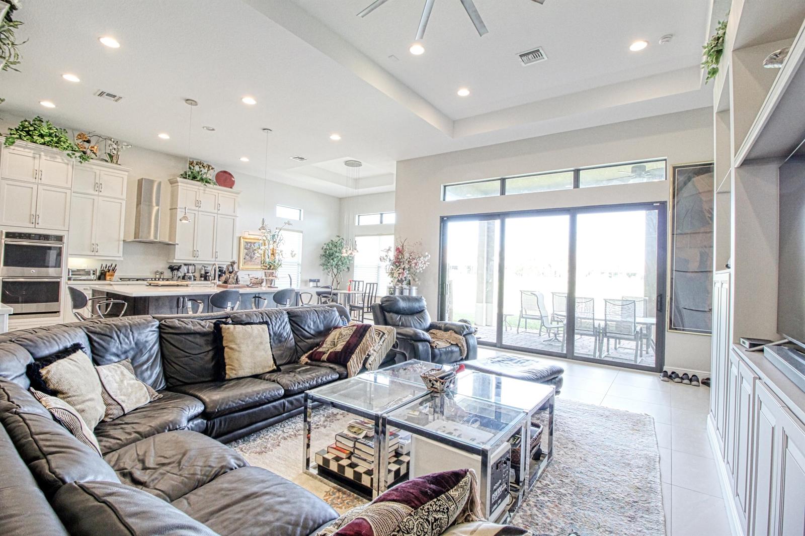 A spacious open-concept living room and kitchen featuring a large leather sectional and glass tables — 12095 Bastille Circle E, Parkland FL 33076, PARKLAND, FL