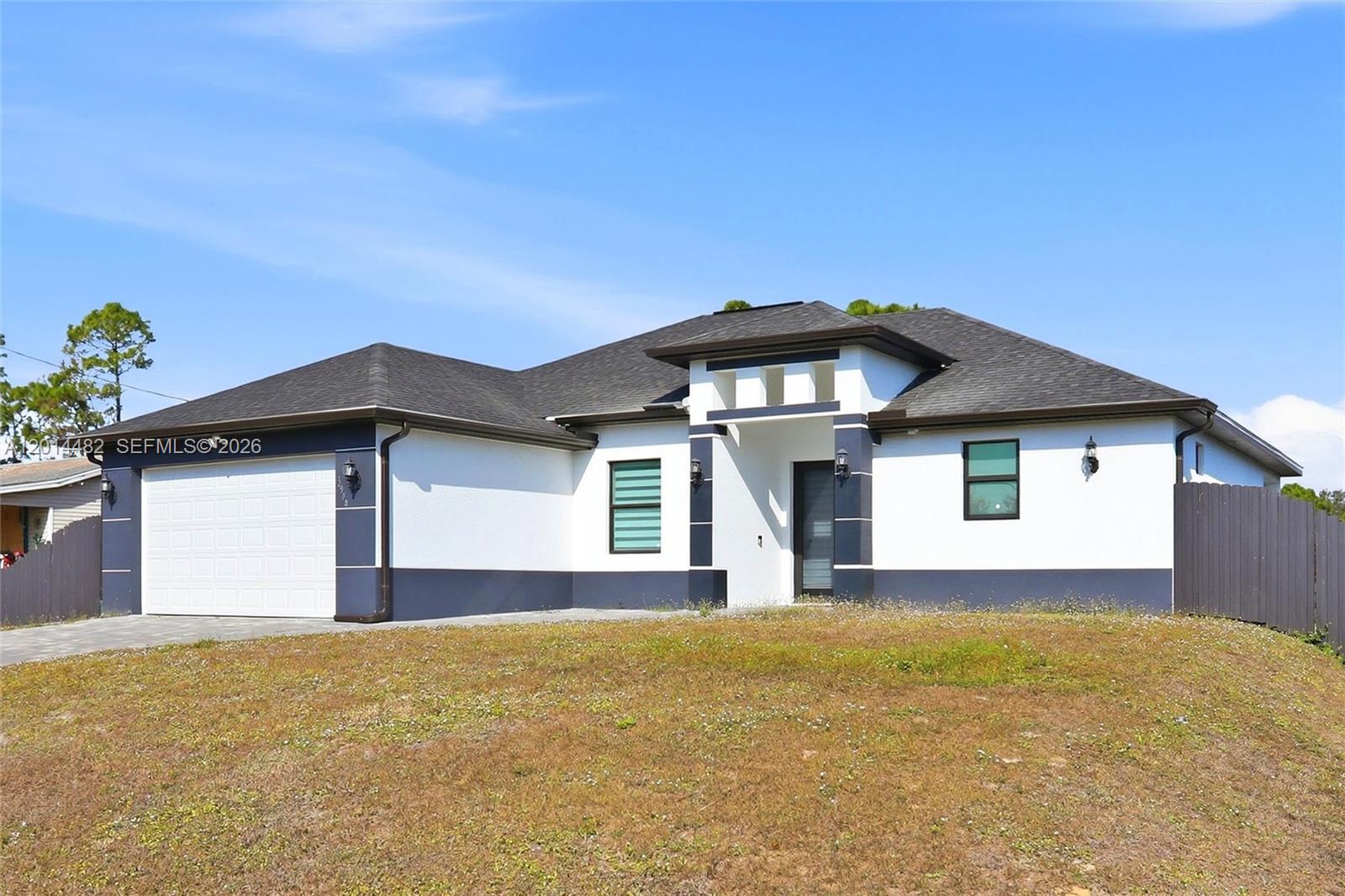 A single-story house with a white stucco exterior, dark trim, and a two-car garage — 2908 SW 9th ST, Lehigh Acres FL 33976, LEHIGH ACRES, FL
