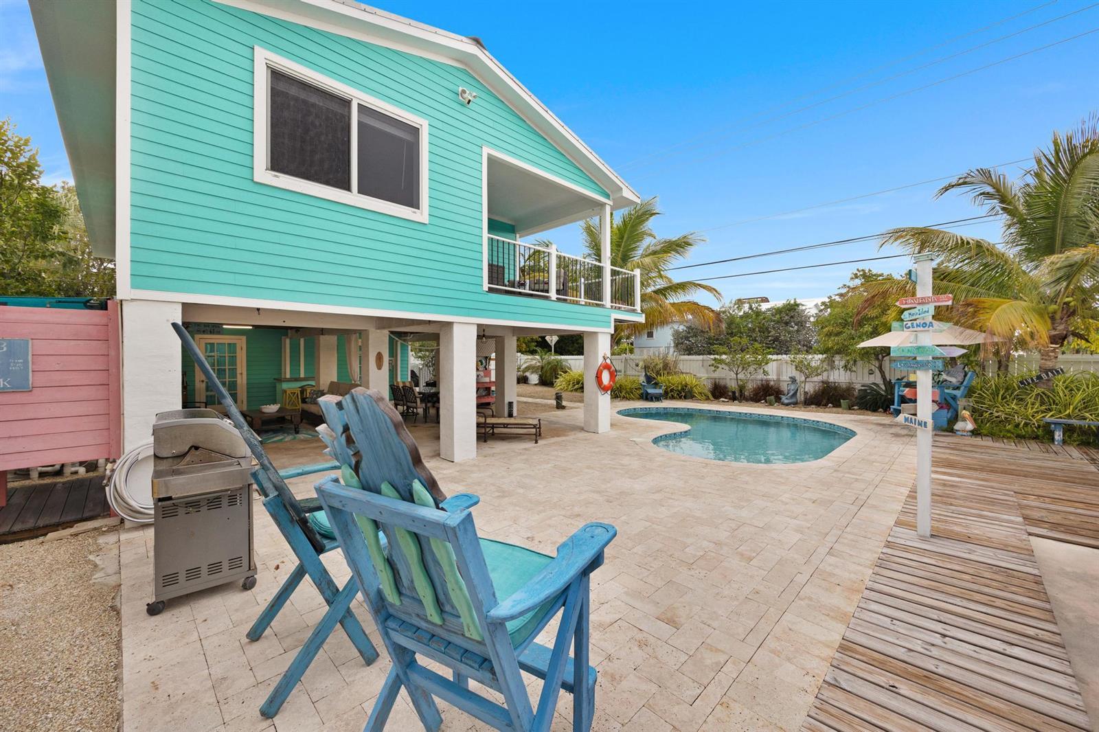 A turquoise elevated house features a backyard patio with a pool and blue wooden chairs — 116 Spanish Main Drive, FL 33042, FL