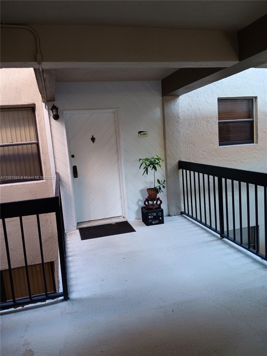 The exterior entrance of a residential unit features a white door, a small plant, and railings — 461 Ives Dairy Rd # 2, Miami FL 33179, MIAMI, FL