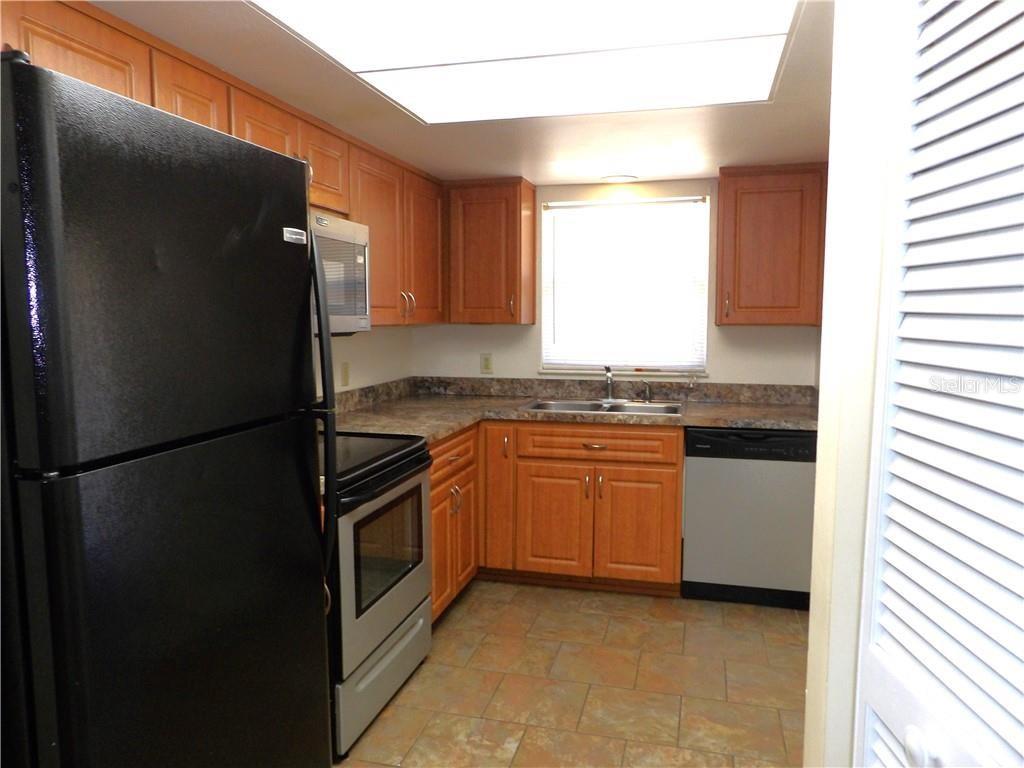 A kitchen features wood cabinets, stainless steel appliances, a double sink, and tile flooring — 1809 COLONADE STREET, INVERNESS, FL