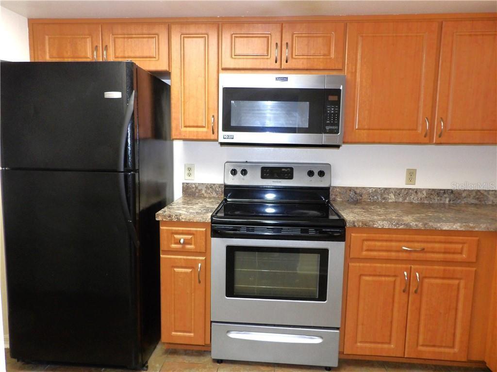 A kitchen features wooden cabinets, a black refrigerator, and stainless steel appliances — 1809 COLONADE STREET, INVERNESS, FL