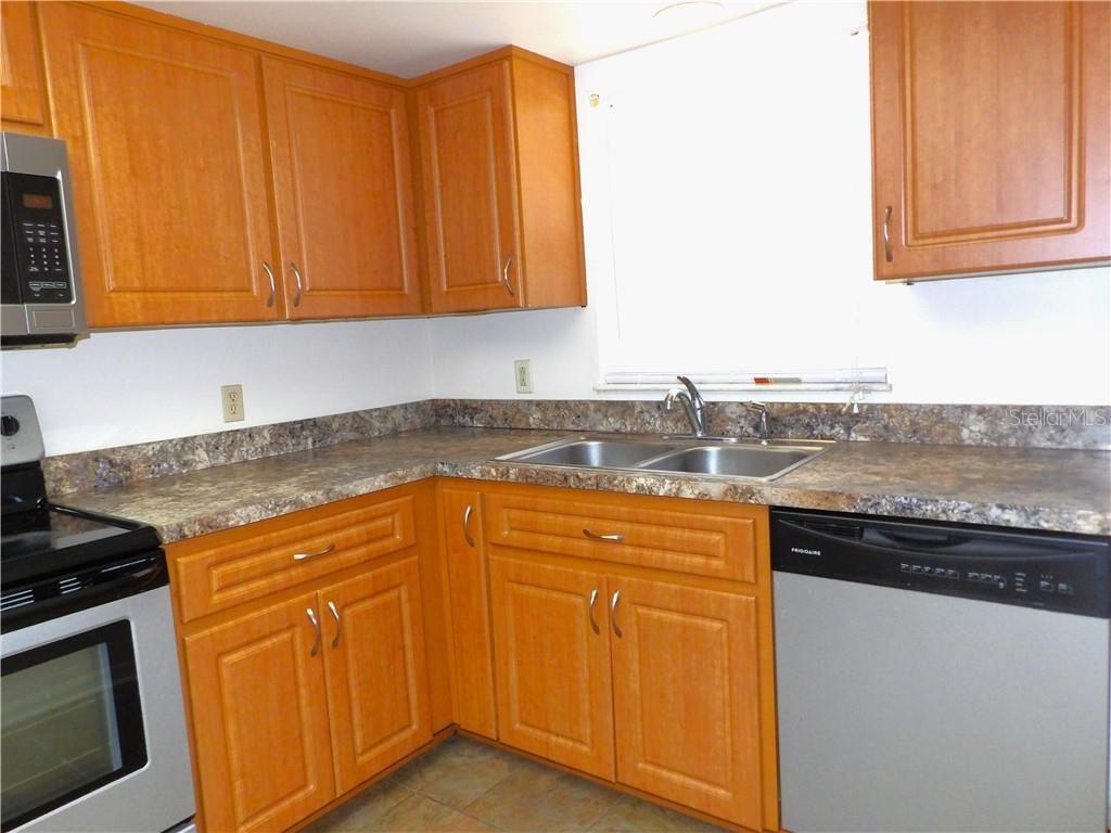 A kitchen features wood cabinets, laminate countertops, a stainless steel dishwasher, and a double sink — 1809 COLONADE STREET, INVERNESS, FL