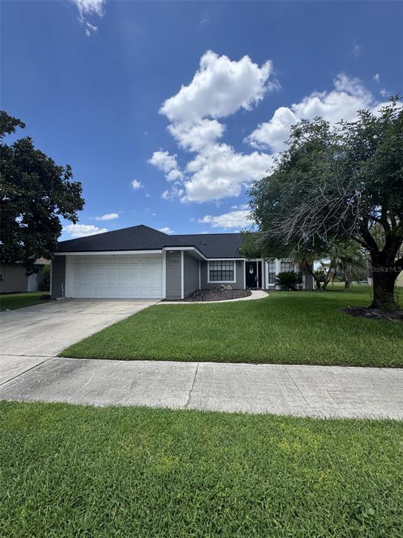 A single-story house with a gray exterior, white garage door, and a large front lawn — 14760 EAGLES CROSSING DRIVE, ORLANDO, FL
