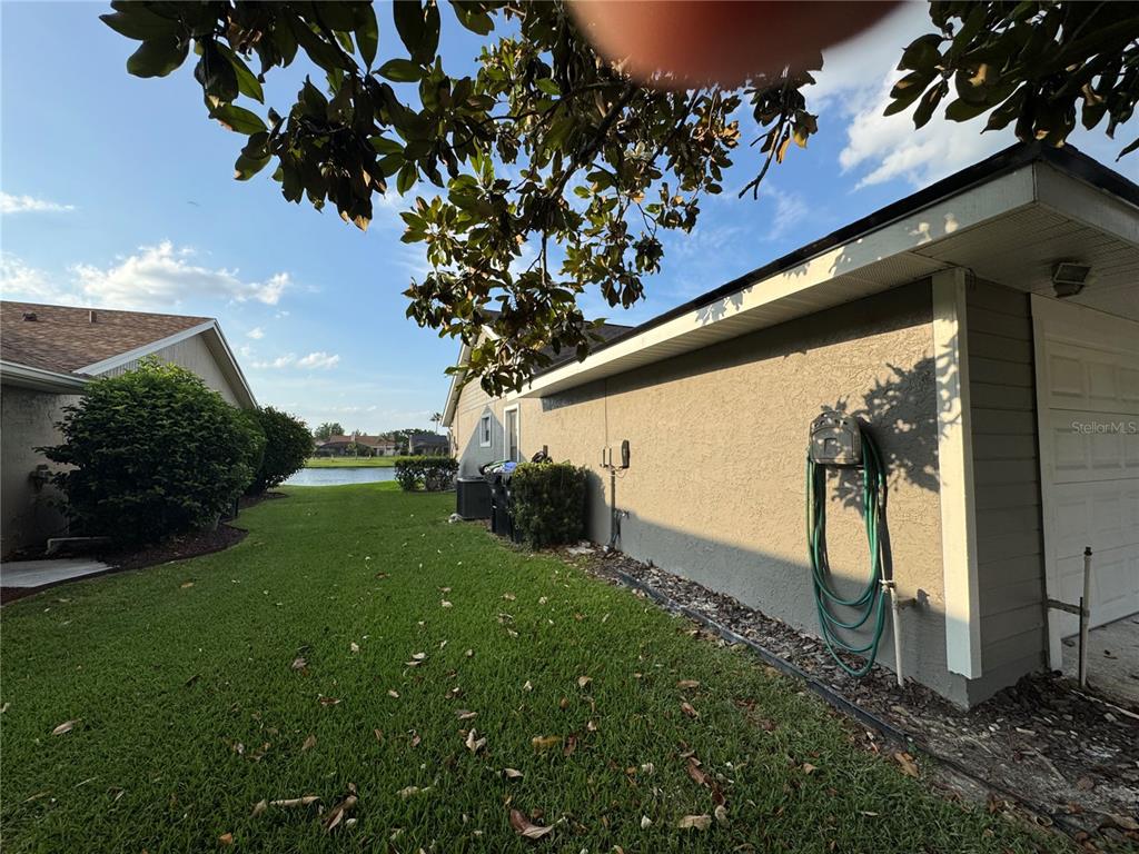 A side view of a house exterior with a lawn, a hose, and a pond — 14760 EAGLES CROSSING DRIVE, ORLANDO, FL