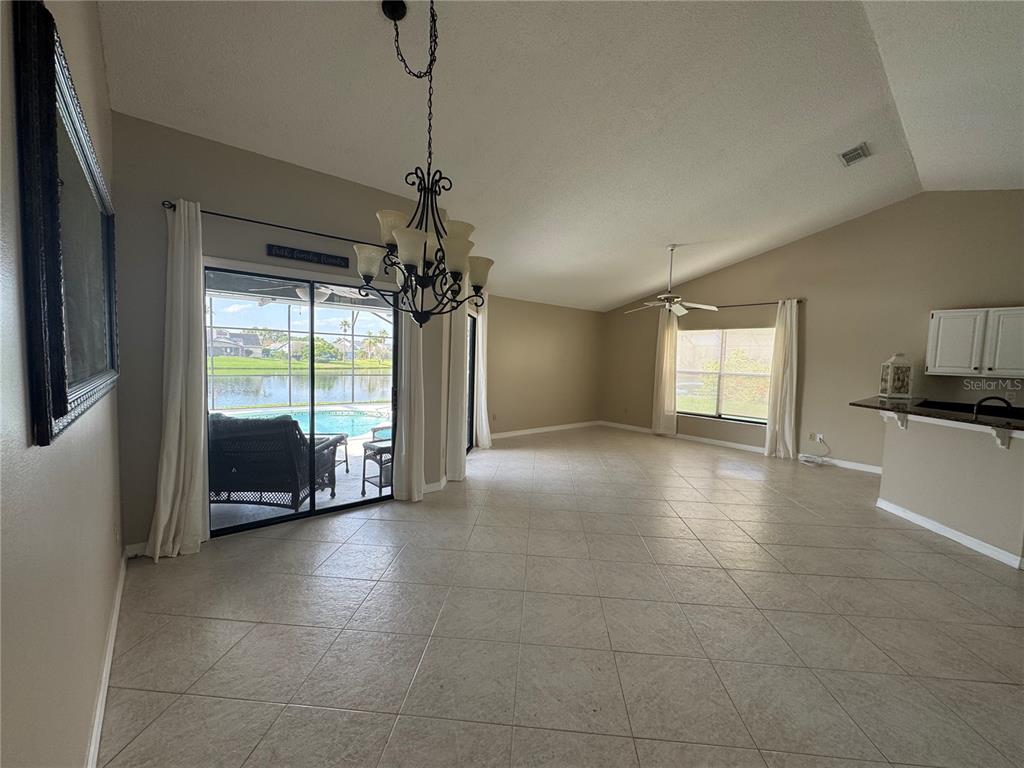 A spacious living area with tile floors, a chandelier, and sliding doors overlooking a pool — 14760 EAGLES CROSSING DRIVE, ORLANDO, FL