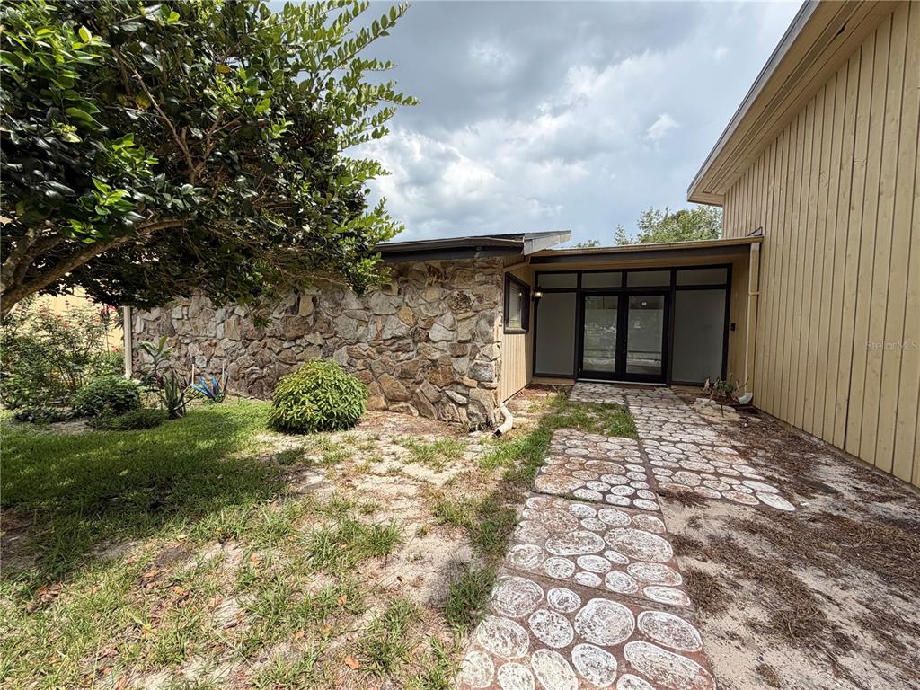 An exterior view of a house featuring a stone wall, a walkway, and a glass-paneled entryway — 6 ROBYN LANE, HAINES CITY, FL