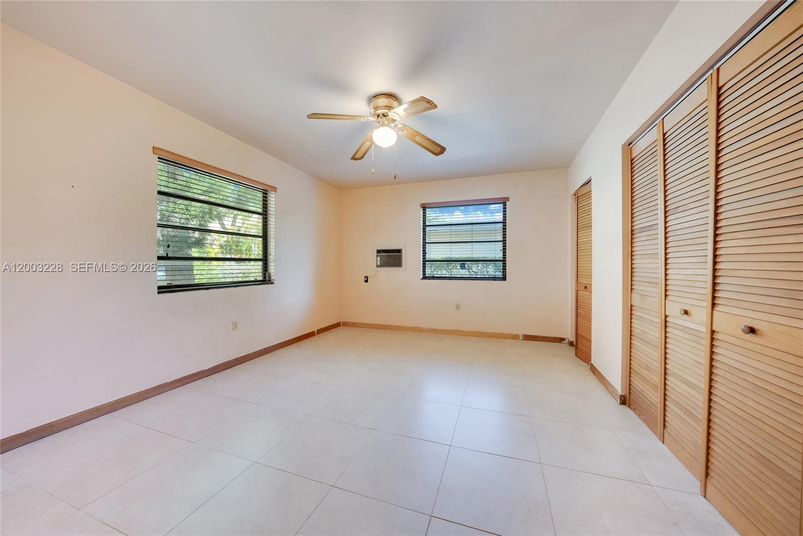 An empty bedroom features light-colored tile flooring, a ceiling fan, and wooden louvered closet doors — 14115 NW 6th Ave, North Miami FL 33168, NORTH MIAMI, FL