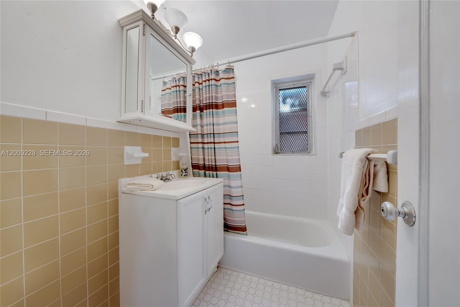 A bathroom features a white vanity, a bathtub with a shower curtain, and tan tiles — 14115 NW 6th Ave, North Miami FL 33168, NORTH MIAMI, FL