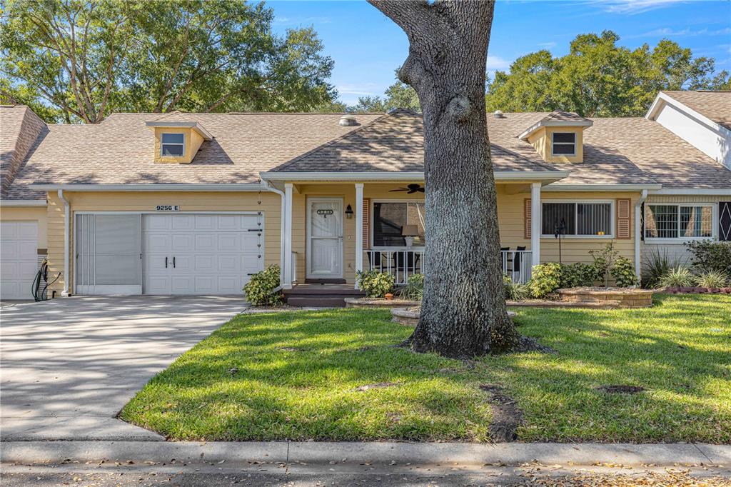 A yellow single-story house features a white garage door, a front porch, and a large tree — 9256 SW 82ND TERRACE UNIT E, OCALA, FL
