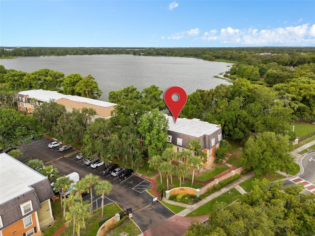An aerial view shows a multi-story apartment building with a parking lot beside a lake — 4190 VERSAILLES DRIVE UNIT 4190D, ORLANDO, FL