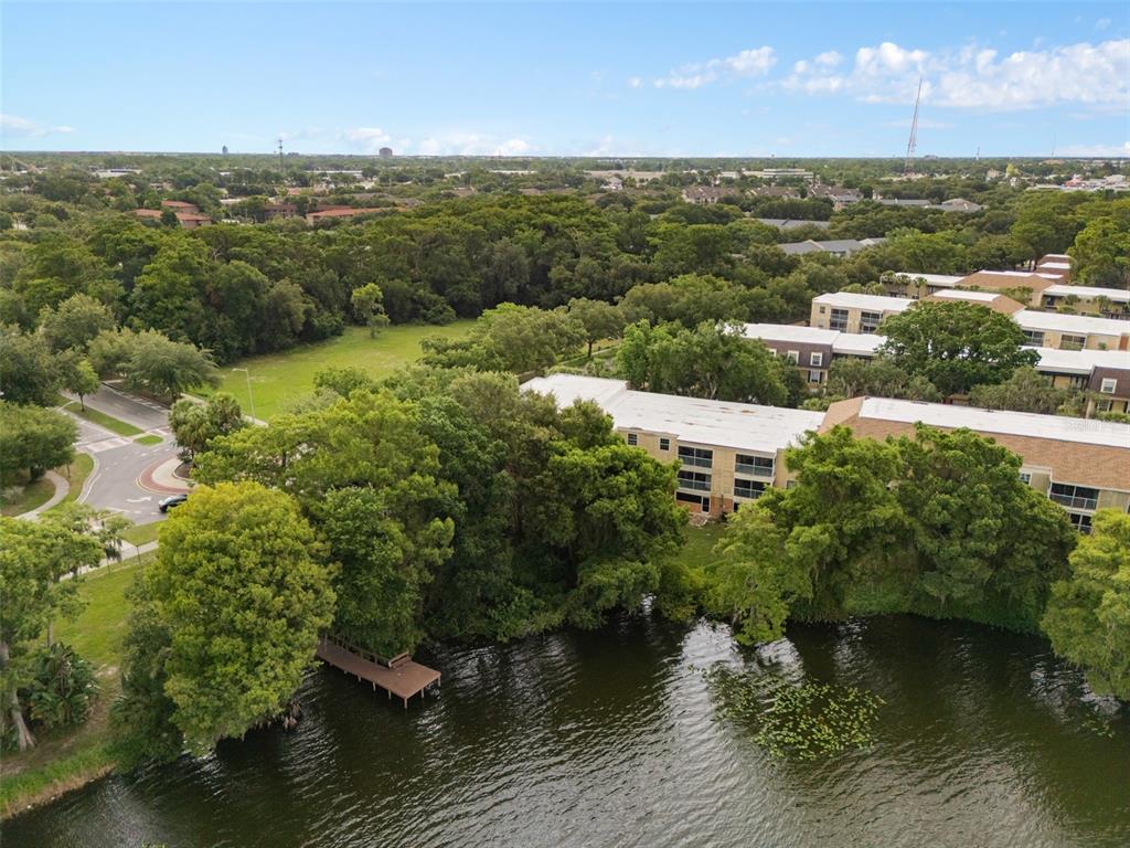 An aerial view shows a multi-story apartment building situated next to a lake and trees — 4190 VERSAILLES DRIVE UNIT 4190D, ORLANDO, FL