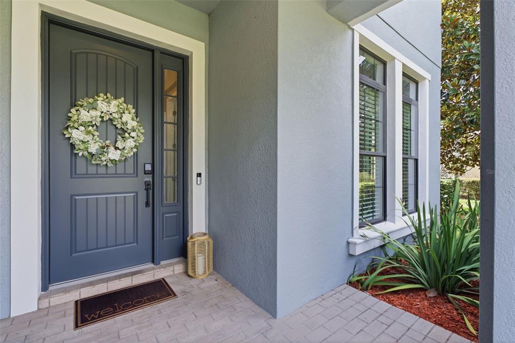 A gray front door with a wreath and a welcome mat sits on a porch — 17909 HOWSMOOR PLACE, LUTZ, FL