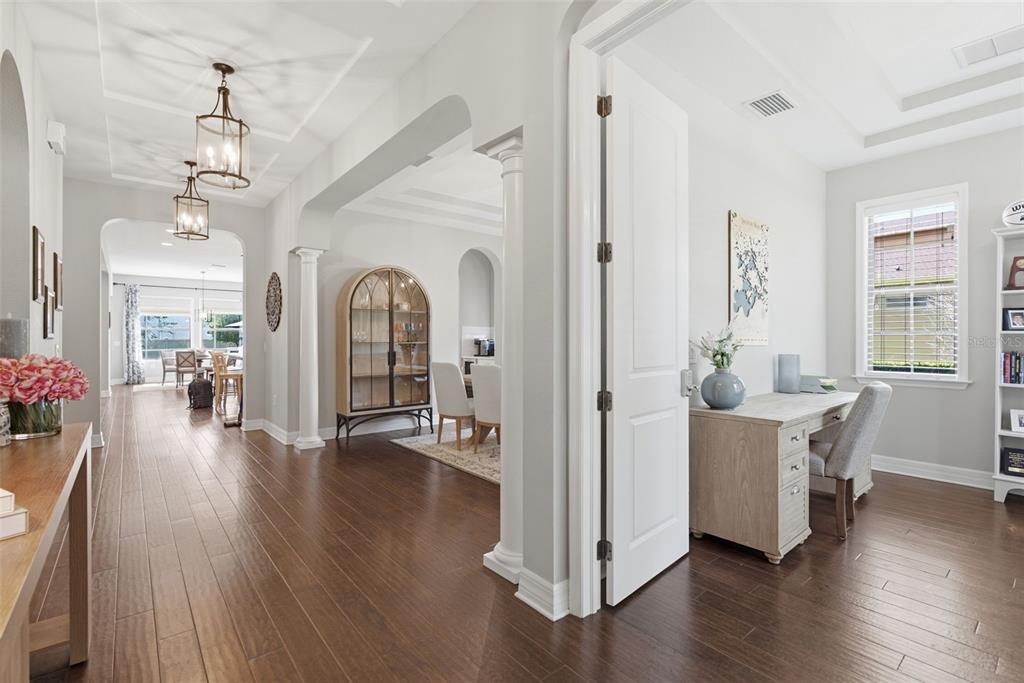 A view from a hallway into a home office and a dining area with wood floors — 17909 HOWSMOOR PLACE, LUTZ, FL