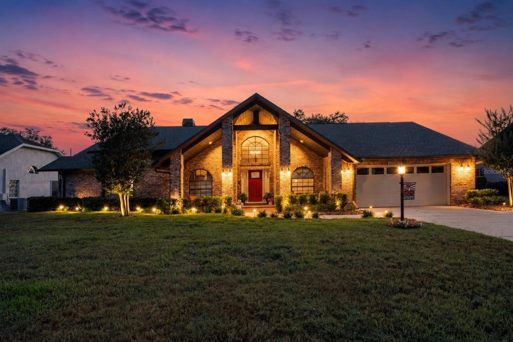 A brick house with a red front door and a two-car garage at sunset — 6219 HUNTINGTON DRIVE, ZEPHYRHILLS, FL