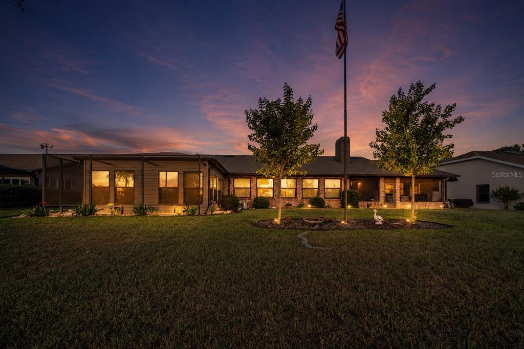 A single-story house with a screened-in porch and a flag pole at sunset — 6219 HUNTINGTON DRIVE, ZEPHYRHILLS, FL