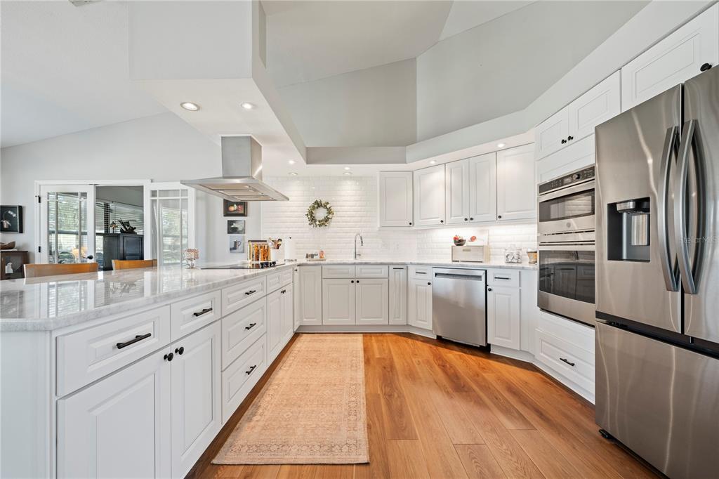 A bright kitchen features white cabinetry, stainless steel appliances, a marble island, and hardwood floors — 6219 HUNTINGTON DRIVE, ZEPHYRHILLS, FL