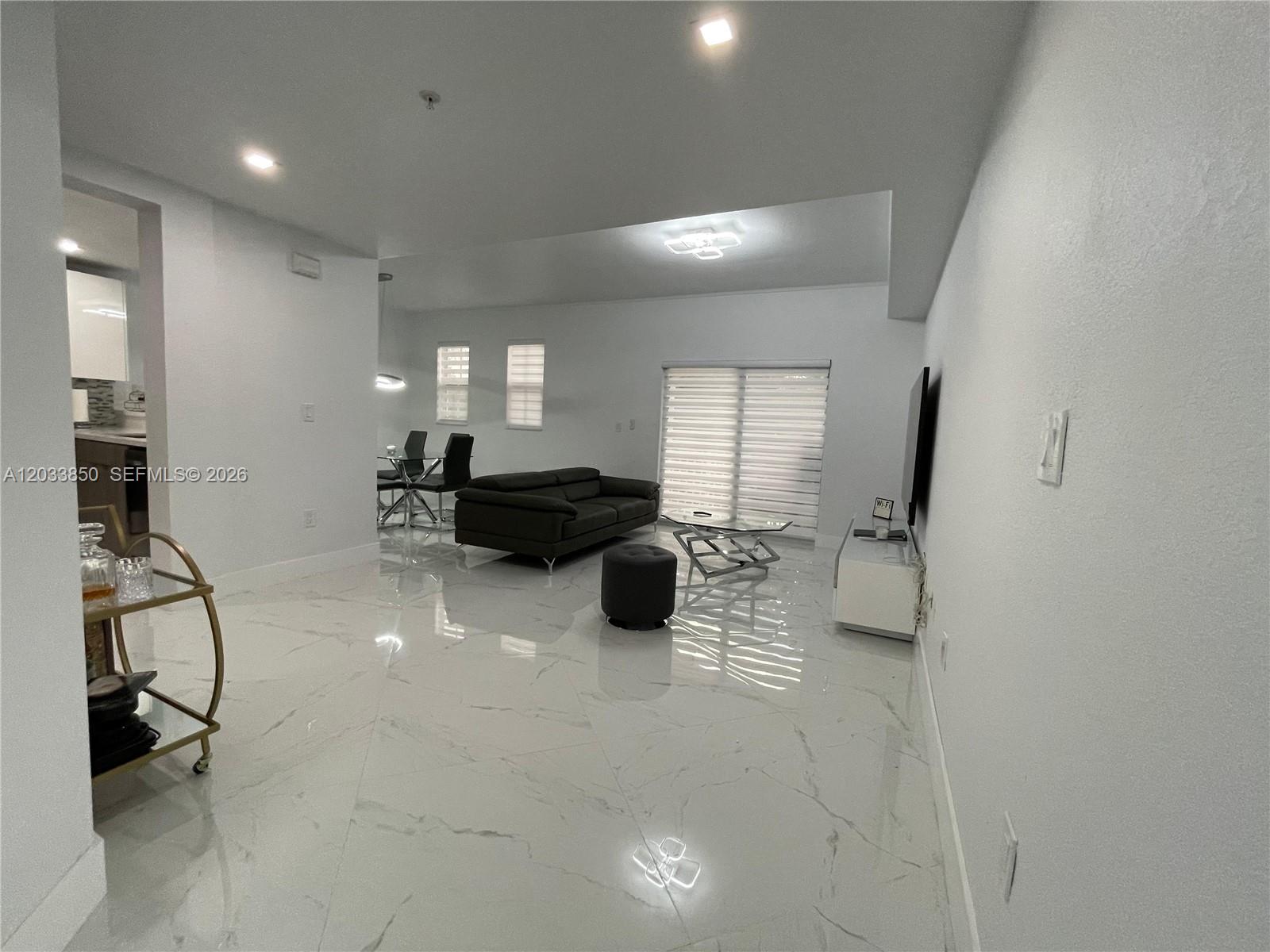 A modern living room features white marble-look tile flooring, a dark sofa, and a television — 10885 NW 89th Ter # 206, Doral FL 33178, DORAL, FL