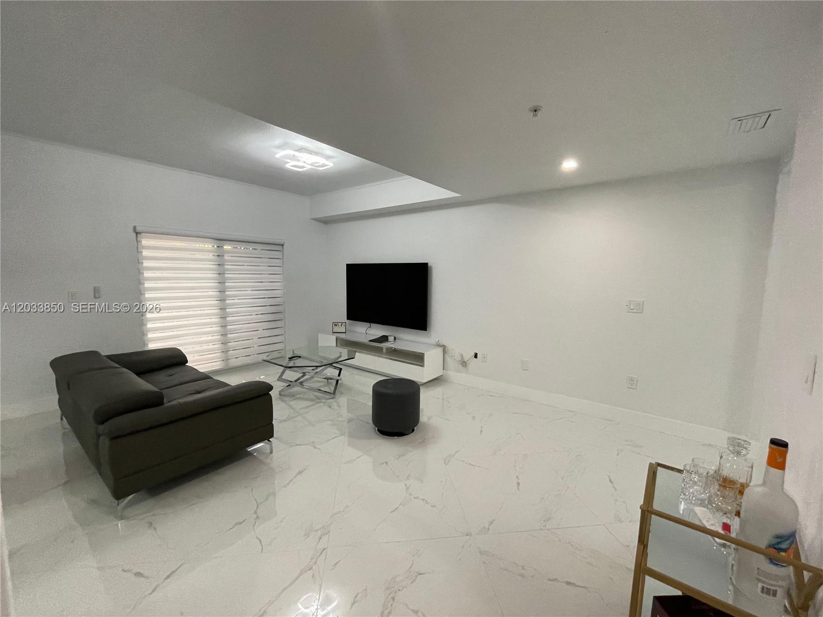 A living room features white marble floors, a dark sofa, and a wall-mounted television — 10885 NW 89th Ter # 206, Doral FL 33178, DORAL, FL