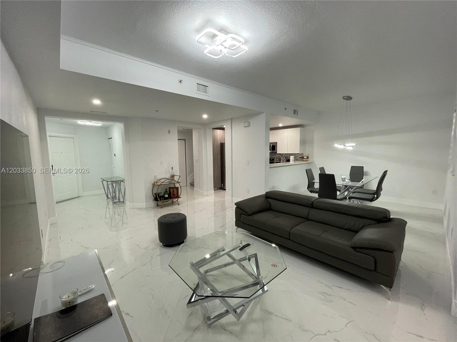 A modern living and dining area features white marble floors, a dark sofa, and glass tables — 10885 NW 89th Ter # 206, Doral FL 33178, DORAL, FL