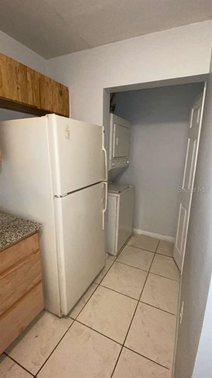 A white refrigerator stands in a kitchen next to a stacked washer and dryer unit — 5214 VIA HACIENDA CIRCLE UNIT A306, ORLANDO, FL