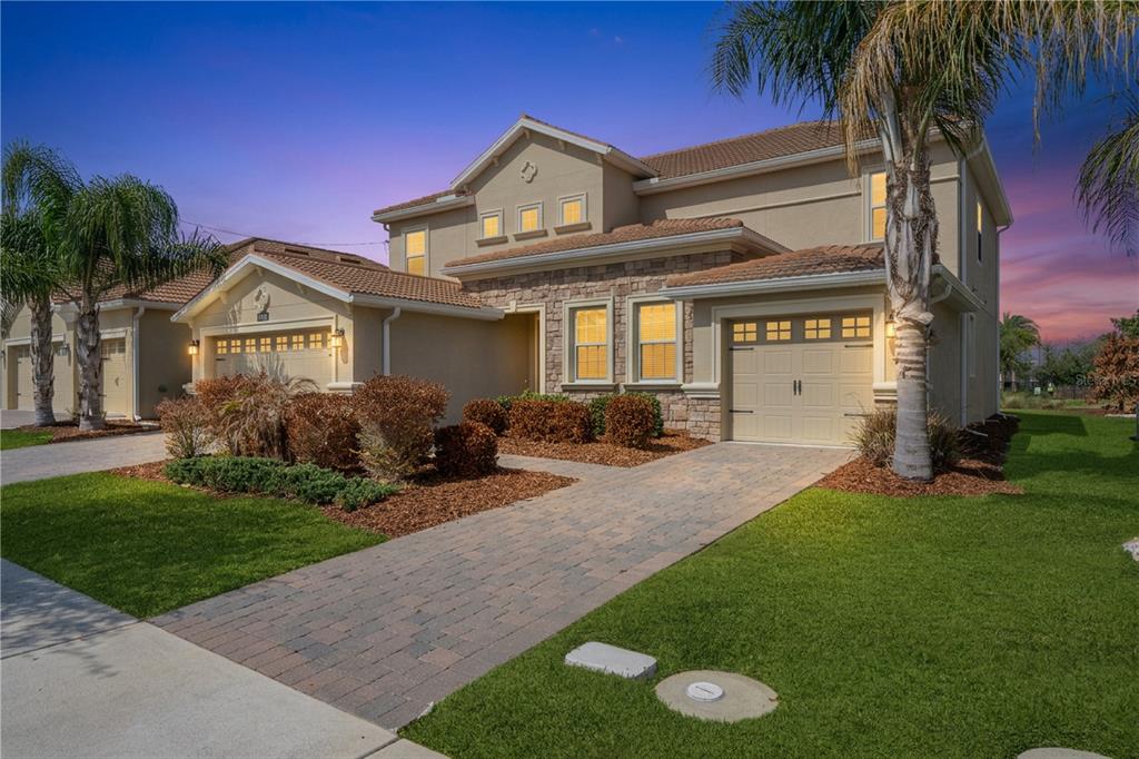 A two-story suburban house with a stone facade, paver driveway, and attached two-car garage — 8995 CROQUET COURT, DAVENPORT, FL