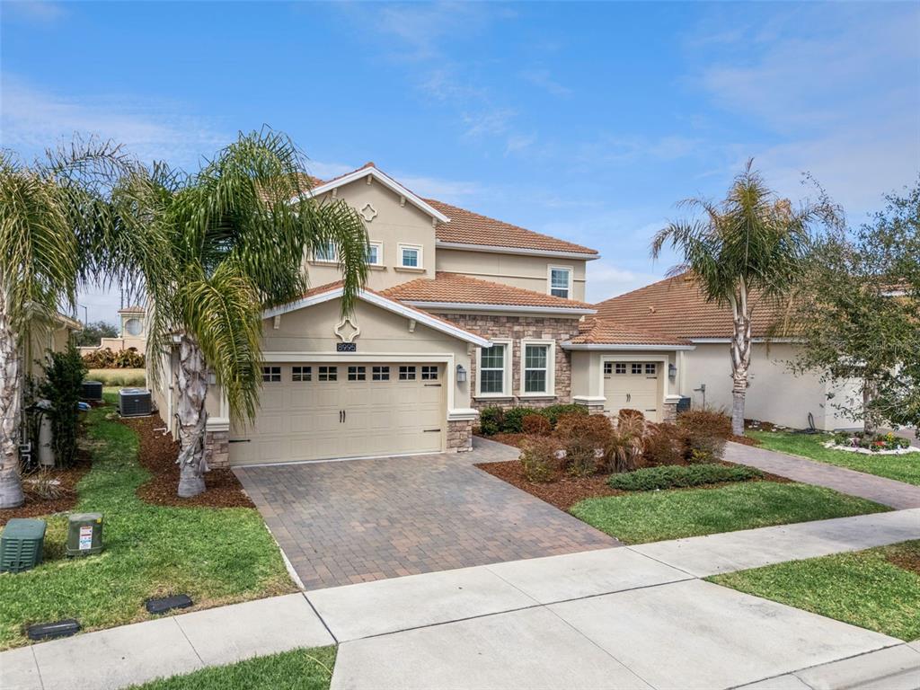 A two-story suburban house with a tan stucco exterior, stone accents, and a tiled roof — 8995 CROQUET COURT, DAVENPORT, FL