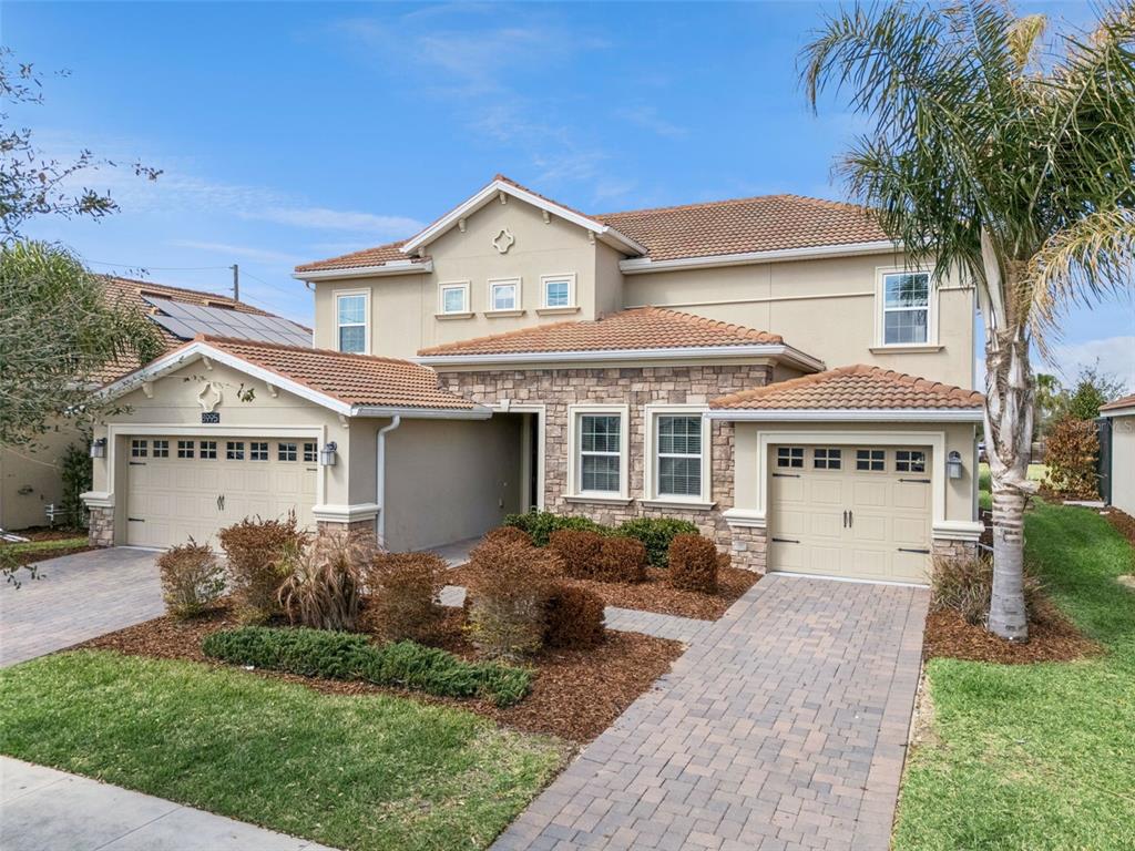 A two-story house with a tile roof, stone facade, and two separate garage doors — 8995 CROQUET COURT, DAVENPORT, FL