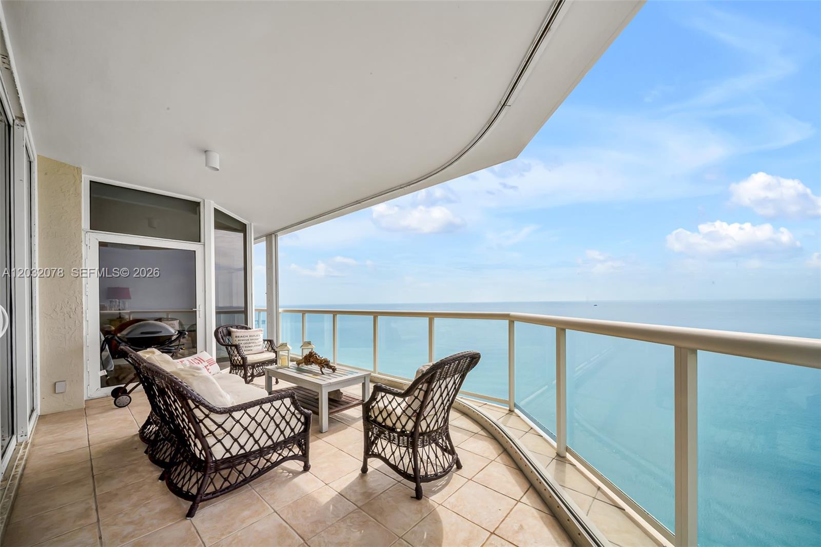 A curved balcony features wicker furniture and a glass railing overlooking the ocean — 6051 N Ocean Dr # 1501, Hollywood FL 33019, HOLLYWOOD, FL
