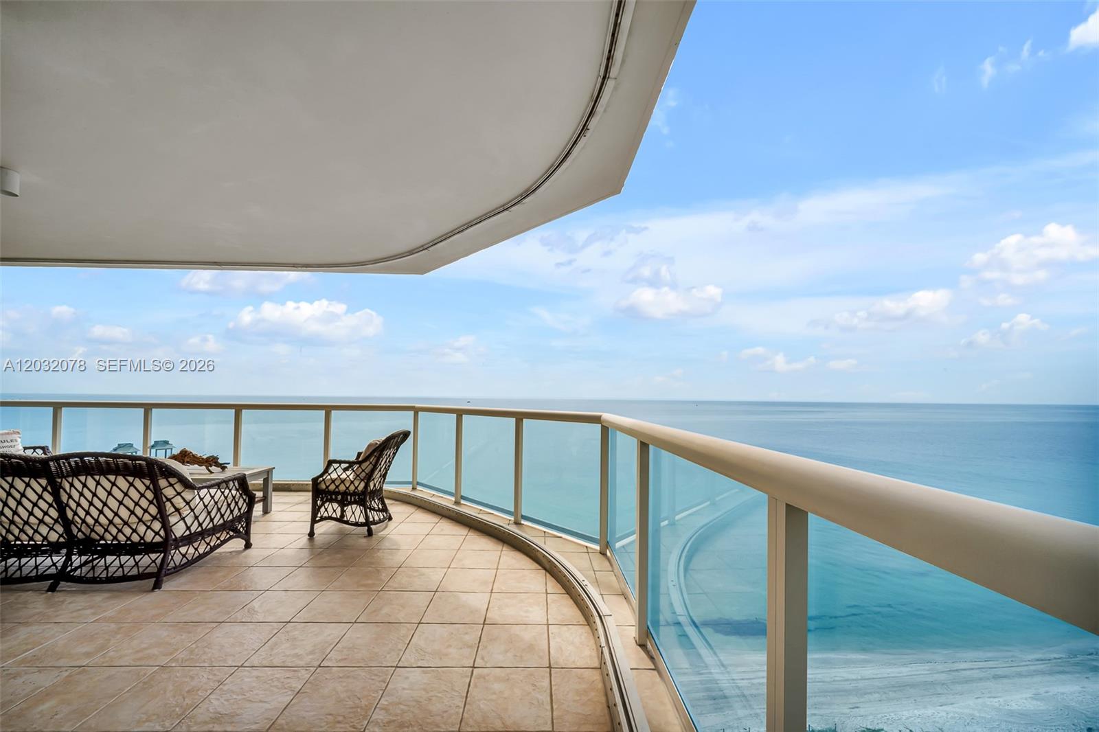 A curved balcony with tile flooring overlooks the ocean with glass railings and patio furniture — 6051 N Ocean Dr # 1501, Hollywood FL 33019, HOLLYWOOD, FL