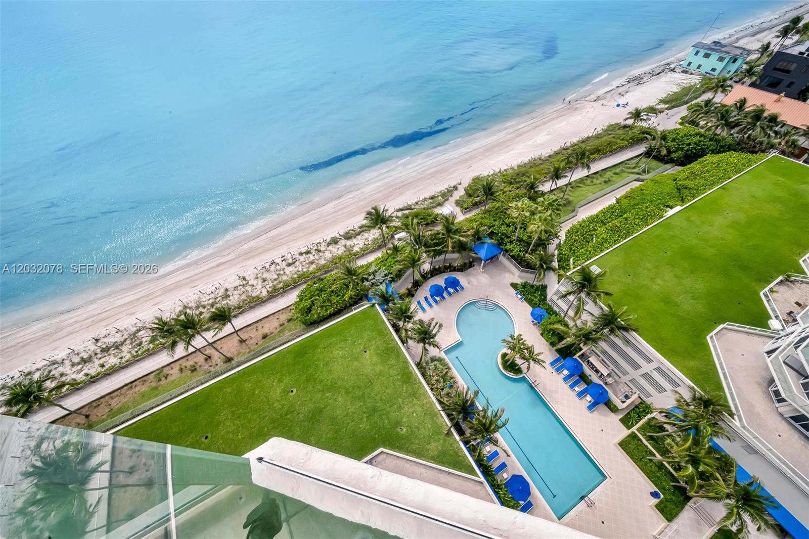 An aerial view shows a swimming pool, green lawn, and beach along the ocean — 6051 N Ocean Dr # 1501, Hollywood FL 33019, HOLLYWOOD, FL
