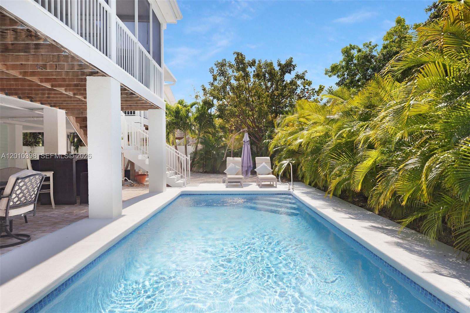 A rectangular swimming pool sits beside a white house with a covered patio and deck — 320 Calzada De Bougainville, Marathon FL 33050, MARATHON, FL