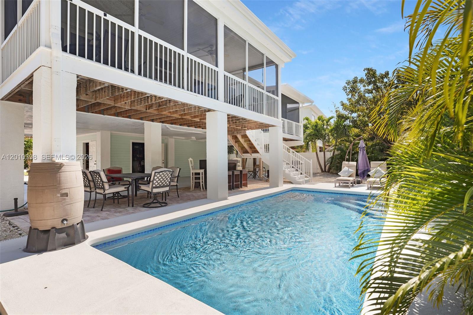 A swimming pool sits beneath the elevated deck of a white house with outdoor seating — 320 Calzada De Bougainville, Marathon FL 33050, MARATHON, FL