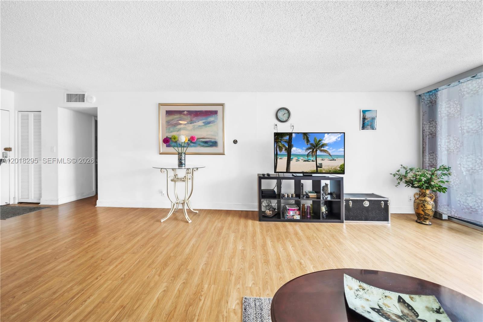 A living room features light wood flooring, white walls, a television console, and a glass table — 2101 S Ocean Dr, Hollywood FL 33019, HOLLYWOOD, FL