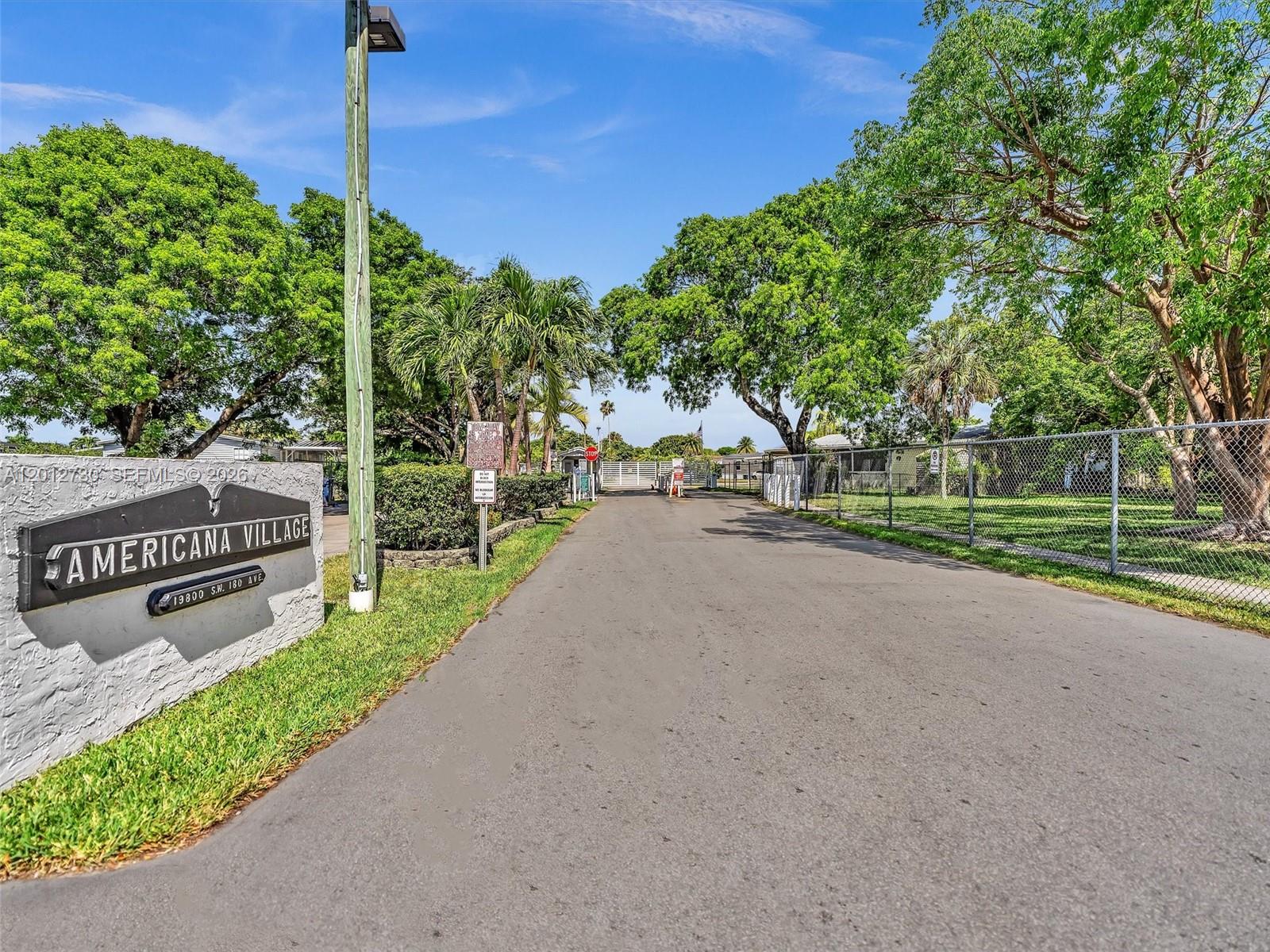The entrance to a residential community features a sign, a paved road, and mature trees — 19800 SW 180th Ave #80, Miami FL 33187, MIAMI, FL