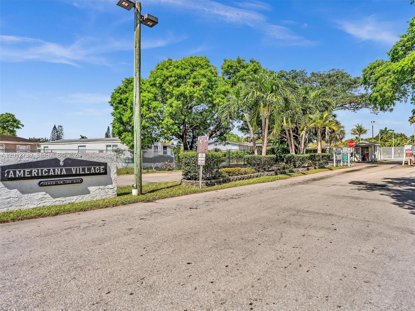 The entrance to a residential community features a stone sign and a paved road — 19800 SW 180th Ave #80, Miami FL 33187, MIAMI, FL
