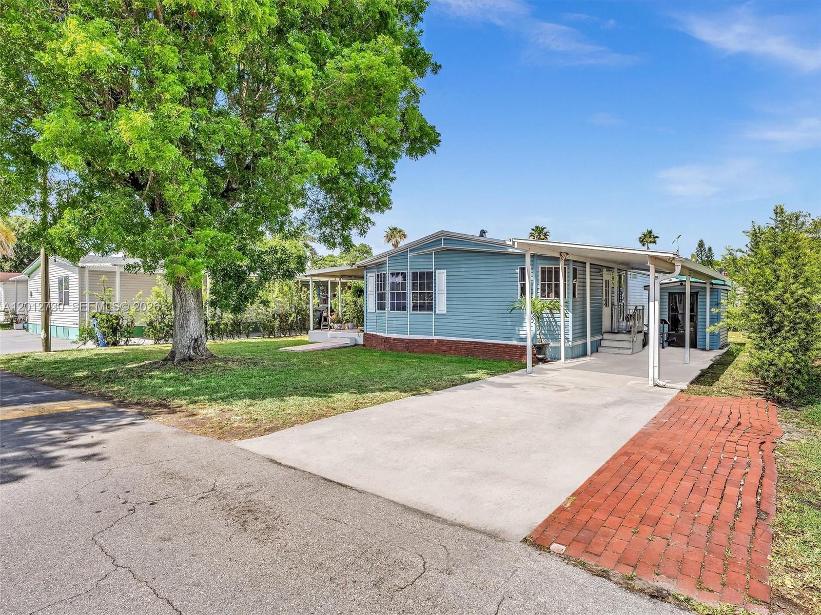 A blue mobile home with a concrete driveway, carport, and a large tree in front — 19800 SW 180th Ave #80, Miami FL 33187, MIAMI, FL