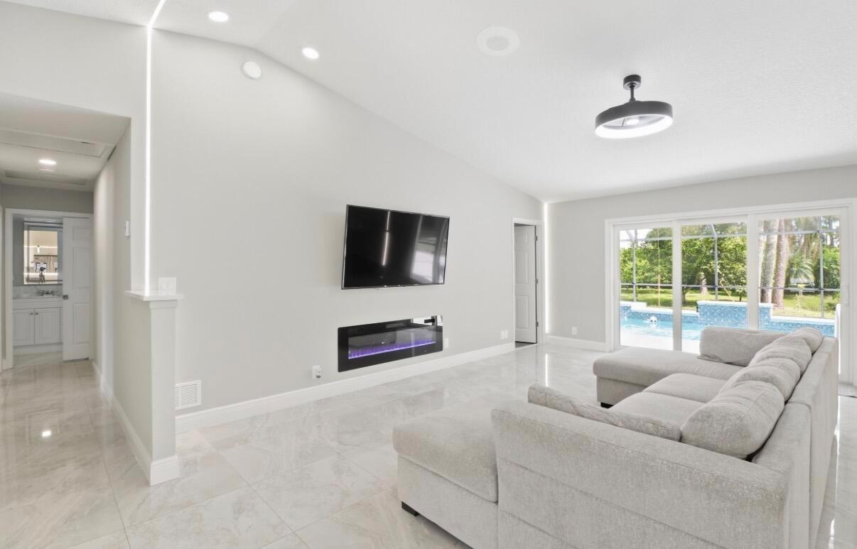 A modern living room features a wall-mounted television, electric fireplace, tile floors, and pool view — 11849 N 59th St Street N, FL 33411, FL