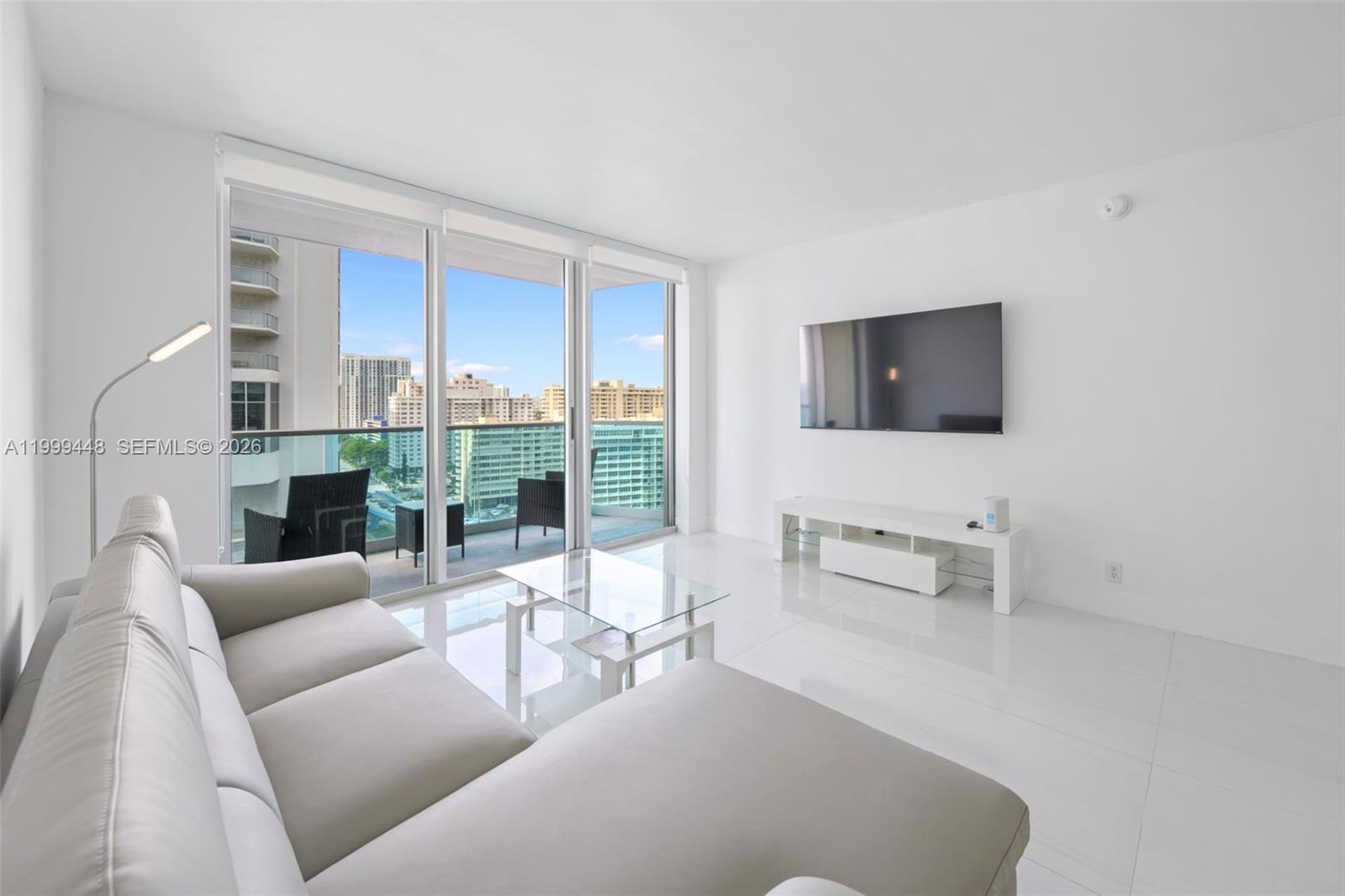 A modern living room features a white sofa, glass coffee table, and a balcony view — 4001 S Ocean Dr # 15B, Hollywood FL 33019, HOLLYWOOD, FL