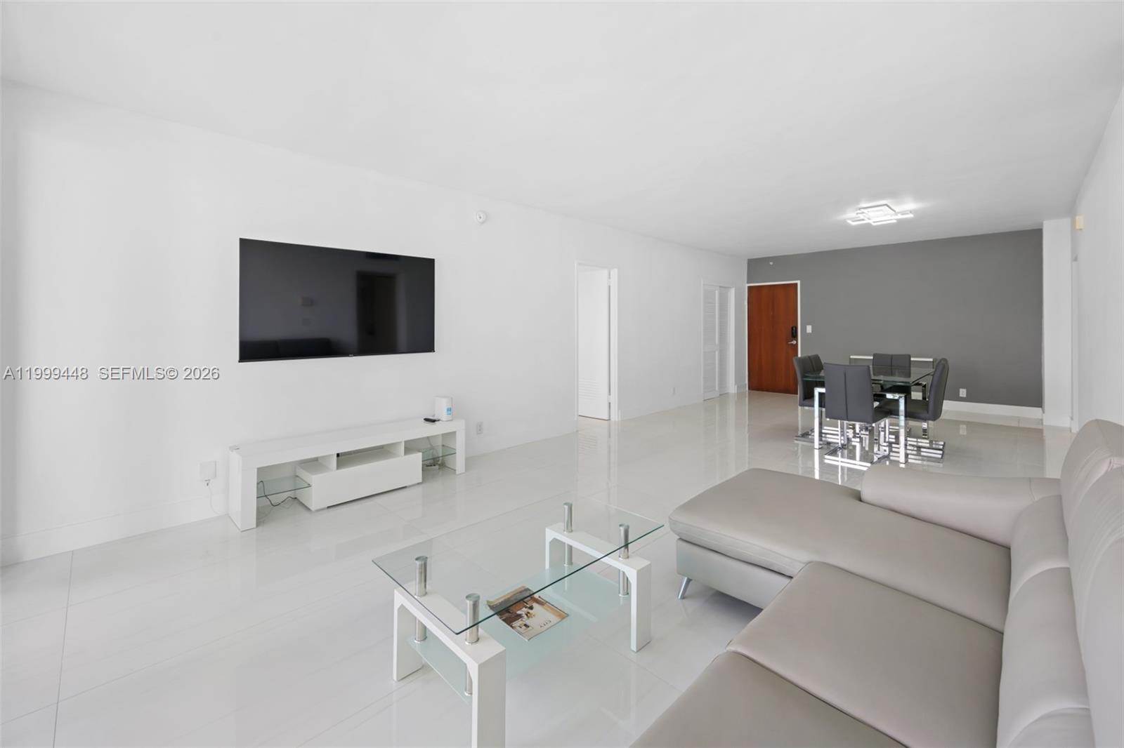 A living and dining area features white tile floors, a wall-mounted television, and modern furniture — 4001 S Ocean Dr # 15B, Hollywood FL 33019, HOLLYWOOD, FL