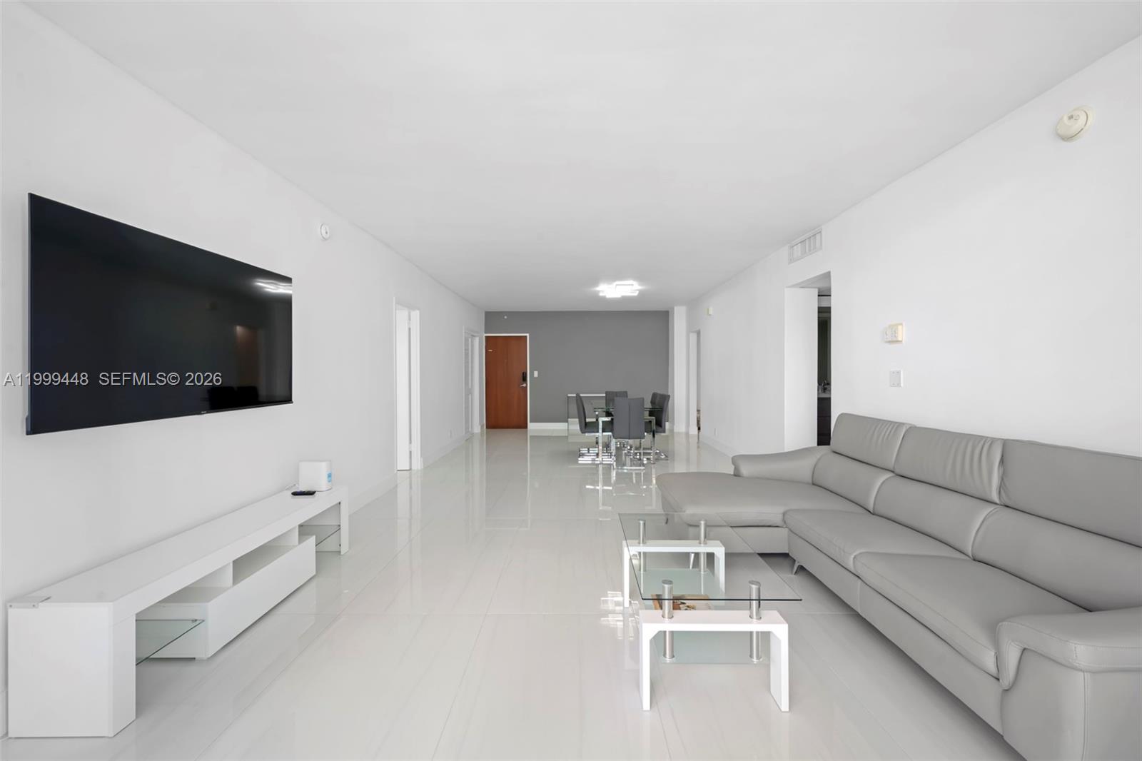 A modern living room features white tile floors, a grey sectional sofa, and a television — 4001 S Ocean Dr # 15B, Hollywood FL 33019, HOLLYWOOD, FL