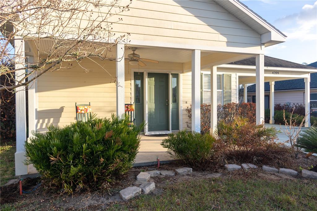 A covered front porch with a green door, ceiling fan, and landscaping in front — 4209 JACARANDA DRIVE, LAKE WALES, FL