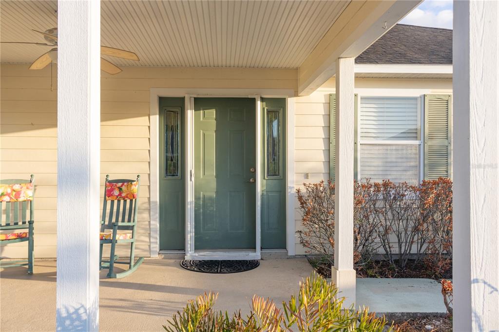A covered porch features a green front door, two rocking chairs, and light-colored siding — 4209 JACARANDA DRIVE, LAKE WALES, FL