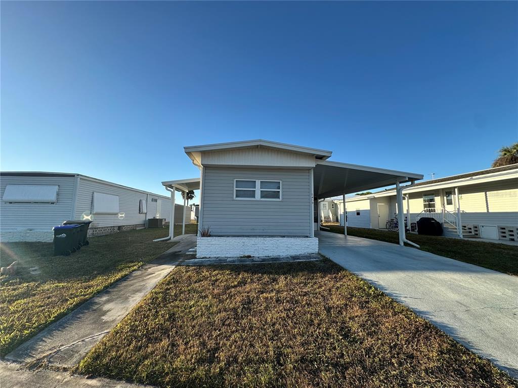 A light gray manufactured home features a white brick planter and an attached carport — 5409 HOLIDAY PARK BOULEVARD, NORTH PORT, FL