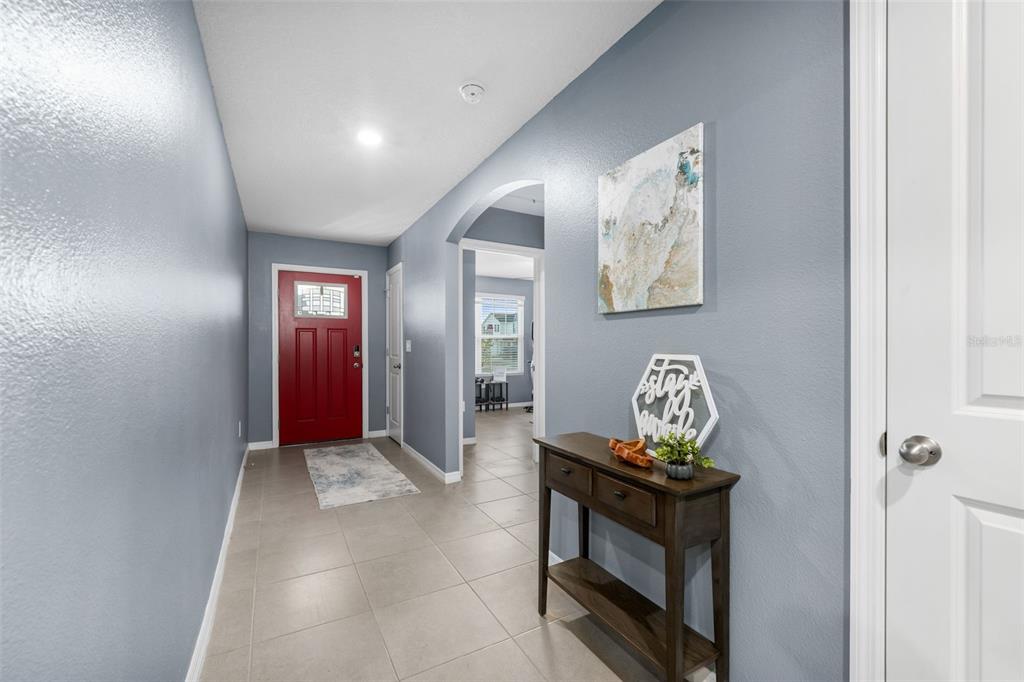 A foyer with light blue walls, tile flooring, a red front door, and a wooden console — 25119 NW 8TH ROAD, NEWBERRY, FL